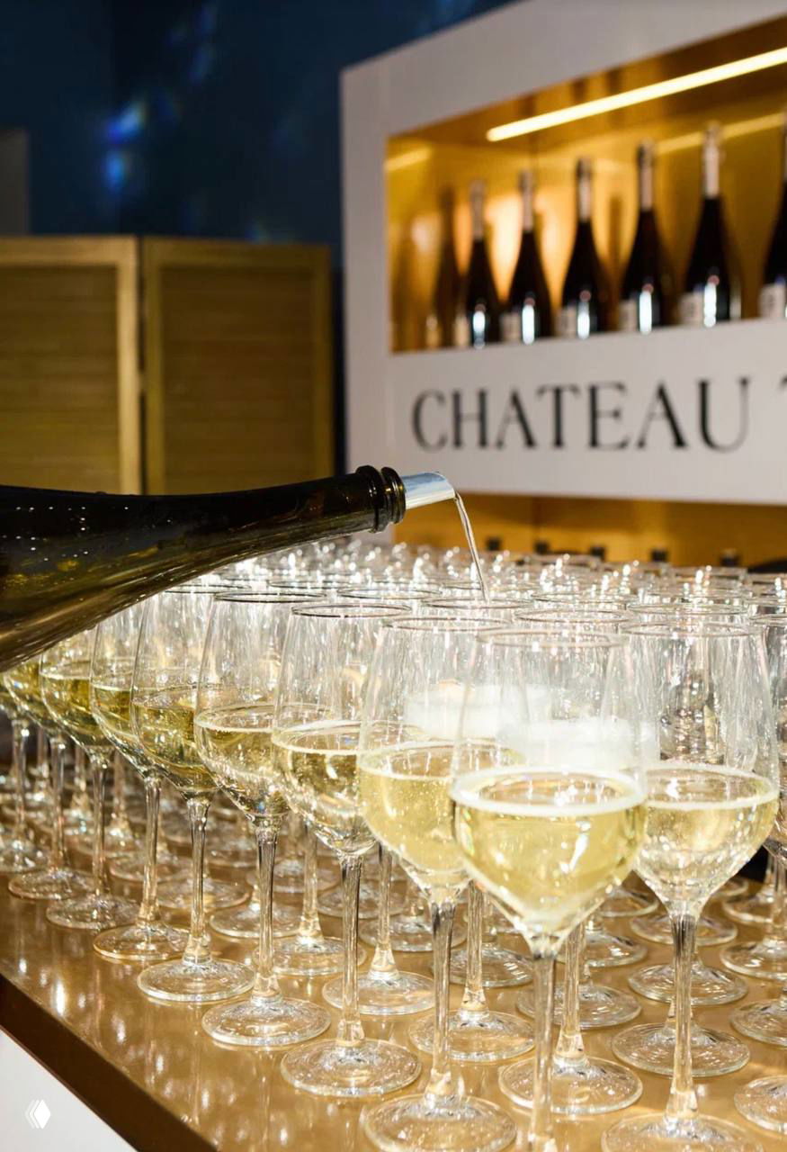 Крупный план подачи игристого вина: множество сервированных бокалов и бутылки на барной стойке Chateau Tamagne в зоне фуршета.