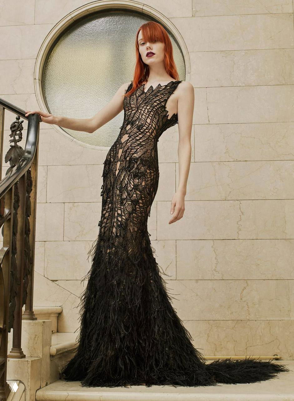 Модель в чёрном кружевном платье с перьями на подоле позирует на лестнице перед мраморной стеной — драматический образ из кампейна Atelier Versace.