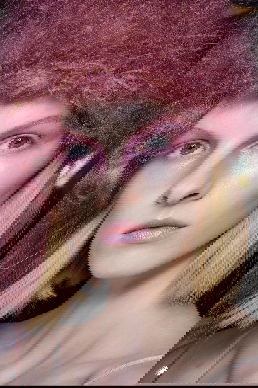 Крупный план модели с розово-лиловыми тенями вокруг глаз и мягким текстурным головным убором; художественный фэшн-кадр с акцентом на цветовой градиент макияжа.