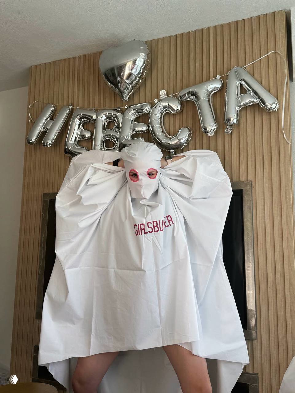 Участница девичника в белой накидке с надписью GIRLSBUSTER и розовыми очками позирует на фоне металлических шаров с буквами «НЕВЕСТА».