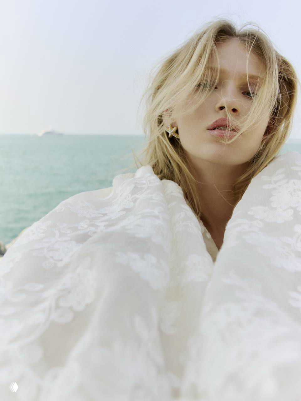 Крупный план модели на фоне моря: белая кружевная ткань окружает лицо, создавая романтичное, прибрежное настроение фотосессии.