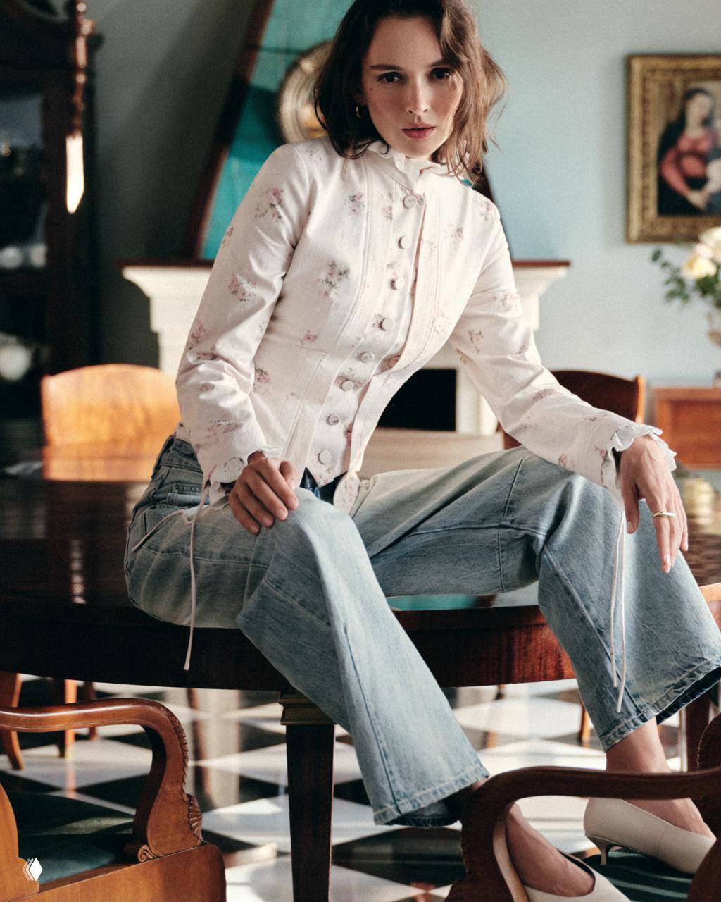 Сидячий портрет: модель в приталенном жакете с тонкими цветочными принтами и джинсах, интерьер с деревянной мебелью и классическим полом.