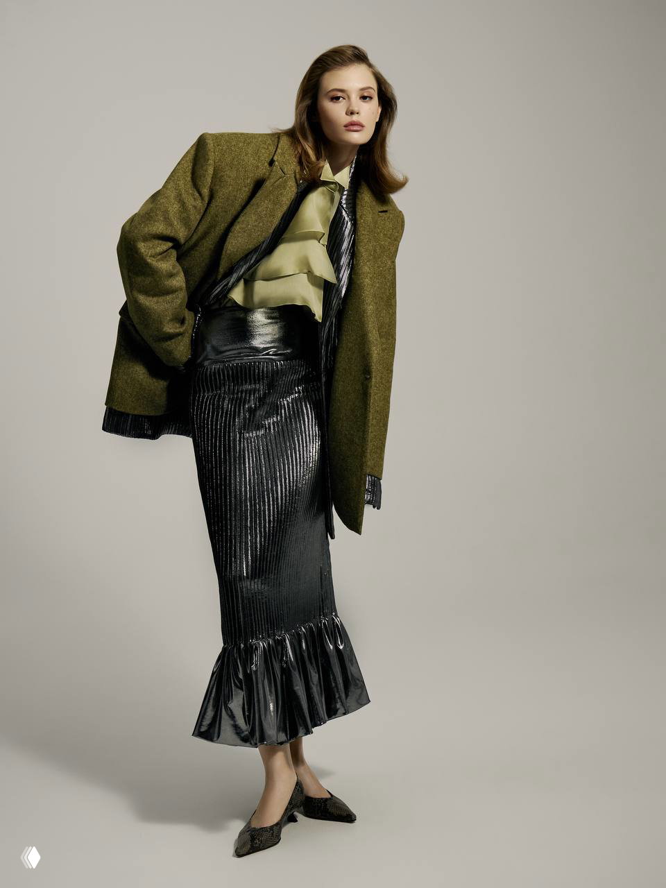 Модель в винтажном по стилю плаще и блестящей юбке позирует в полный рост: сочетание классики и современного кроя в редакционном кадре.