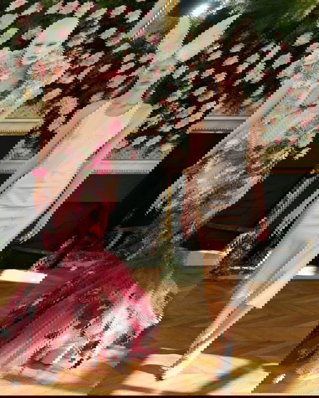 Коллаж с показом: слева модель в цветочном платье с корсетом и розами, справа — лаконичное кремовое платье с похожим крылатым головным убором на фоне стены из роз.