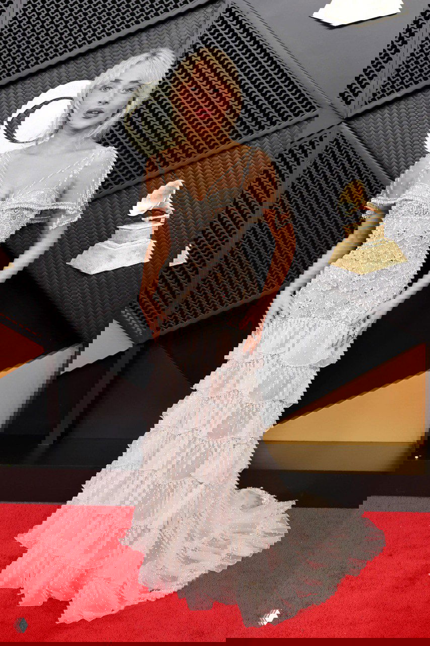 Лёгкое многоярусное светлое платье с прозрачными элементами и нежной отделкой на красной дорожке, женственный романтичный образ в полный рост.