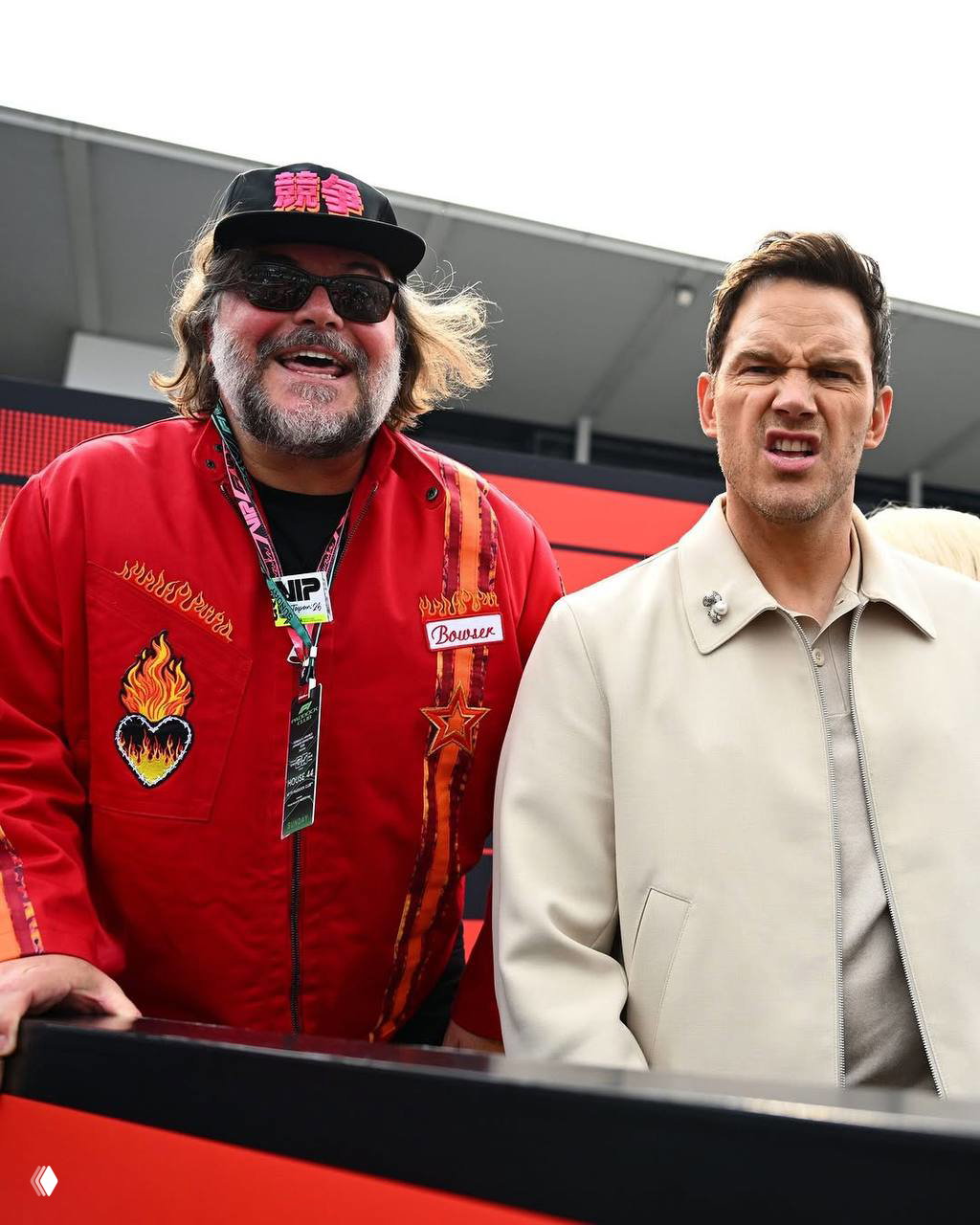 Два человека в кадре крупным планом у барьера трассы: один в светлой куртке, другой в красной куртке — реакция и эмоции публики на гонке