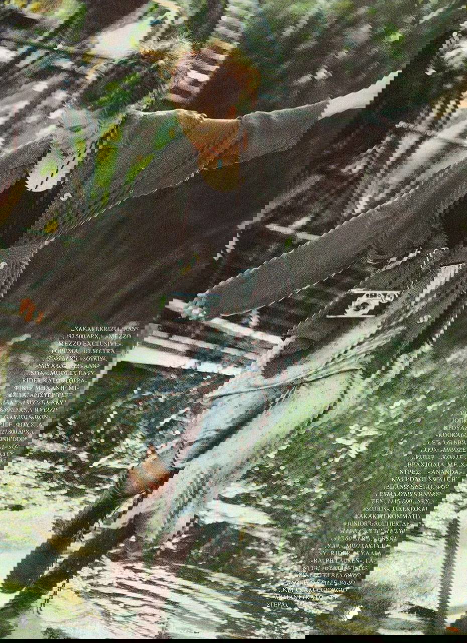 Модель в свободном жакете и длинной юбке балансирует у воды, с камерой на шее — динамичный образ винтажной летней съёмки для журнала.