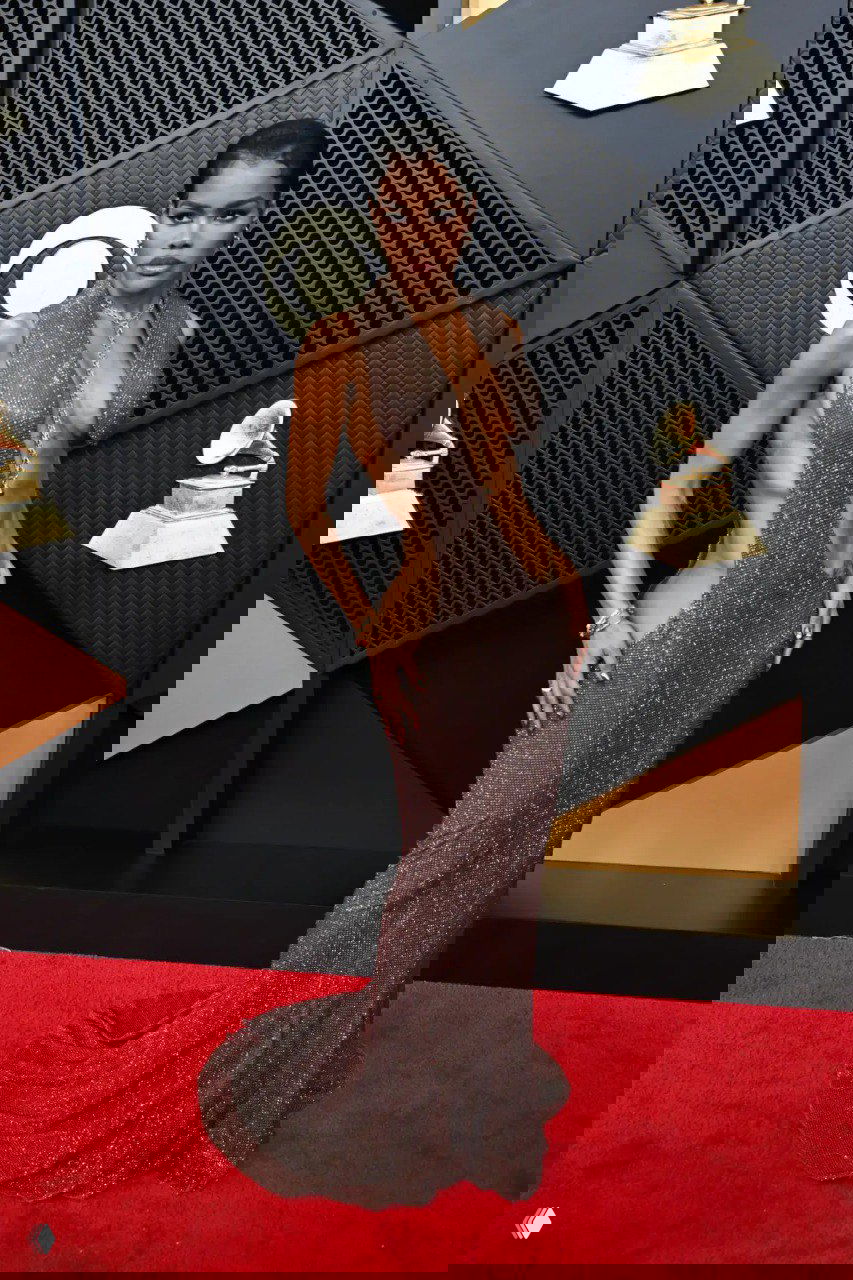 Глиттерное коричнево‑золотистое платье с глубокими вырезами и блеском ткани на красной дорожке, смелый сексуальный силуэт и минимальные аксессуары.