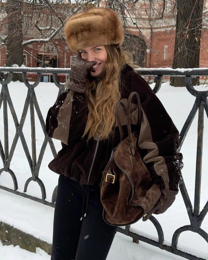 Модель в большой меховой шапке и тёплой куртке на фоне заснеженного парка — образ в славянском стиле с акцентом на тепло и текстуру меха.