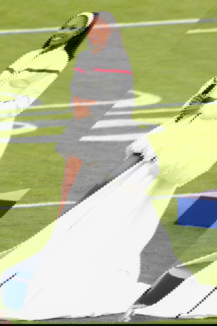 Исполнительница в объёмном белом платье с длинным шлейфом держит микрофон на футбольном поле во время церемонии, видна разметка поля и часть трибун