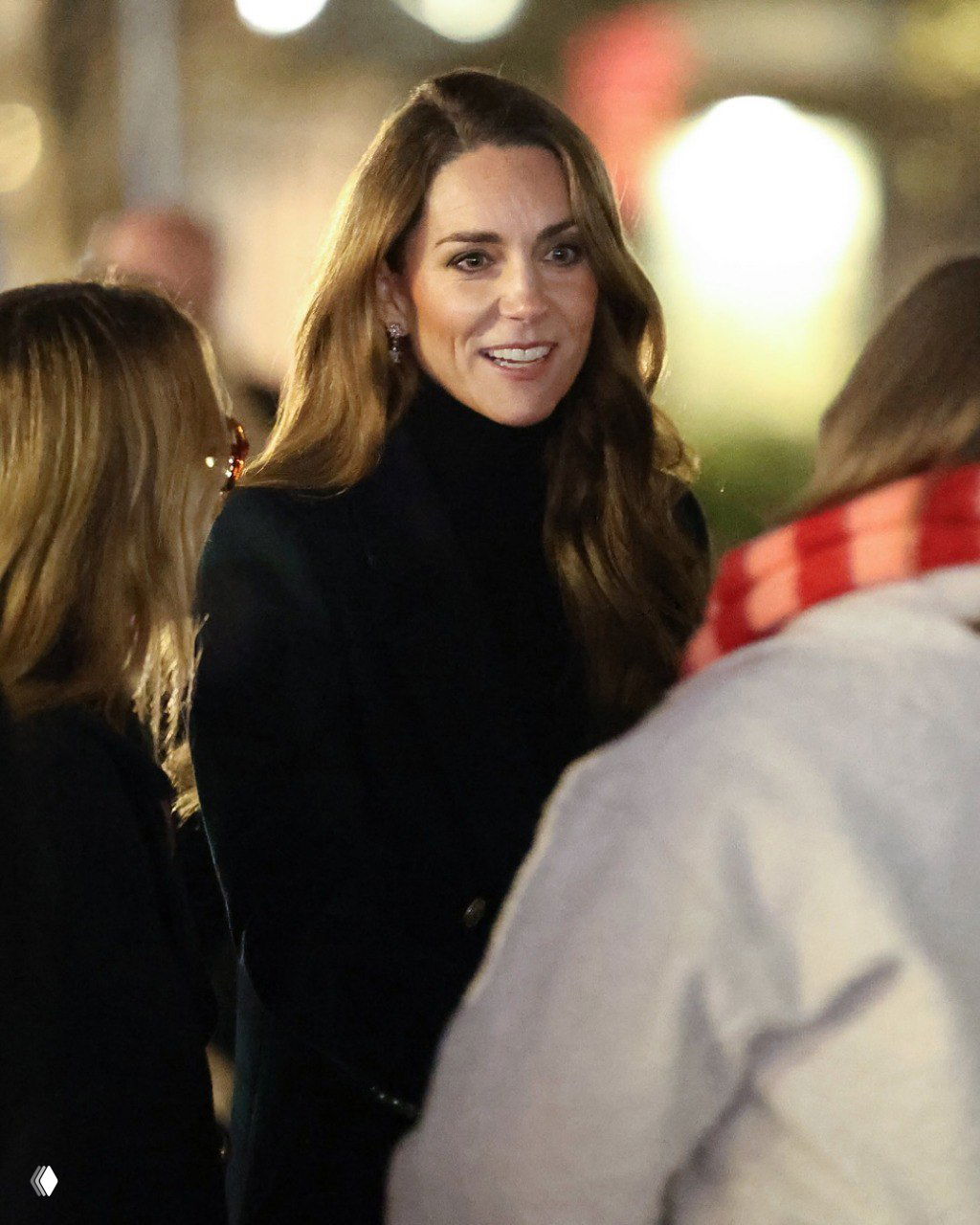 Принцесса Кейт общается с гостями в саду Ever After Garden на фоне размытых огней и вечерней атмосферы благотворительного вечера.