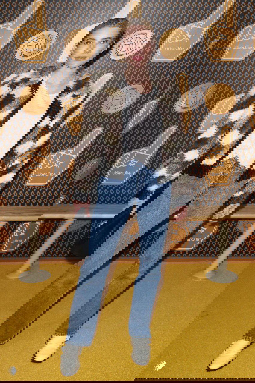 Женщина в шубе в шахматную клетку поверх базовой футболки и джинсов позирует на фотозоне, кадр подчёркивает повседневный модный образ гостя