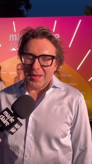 Крупный план Андрея Малахова в белой рубашке у яркого стенда Marie Claire на Blogger Party, держит микрофон