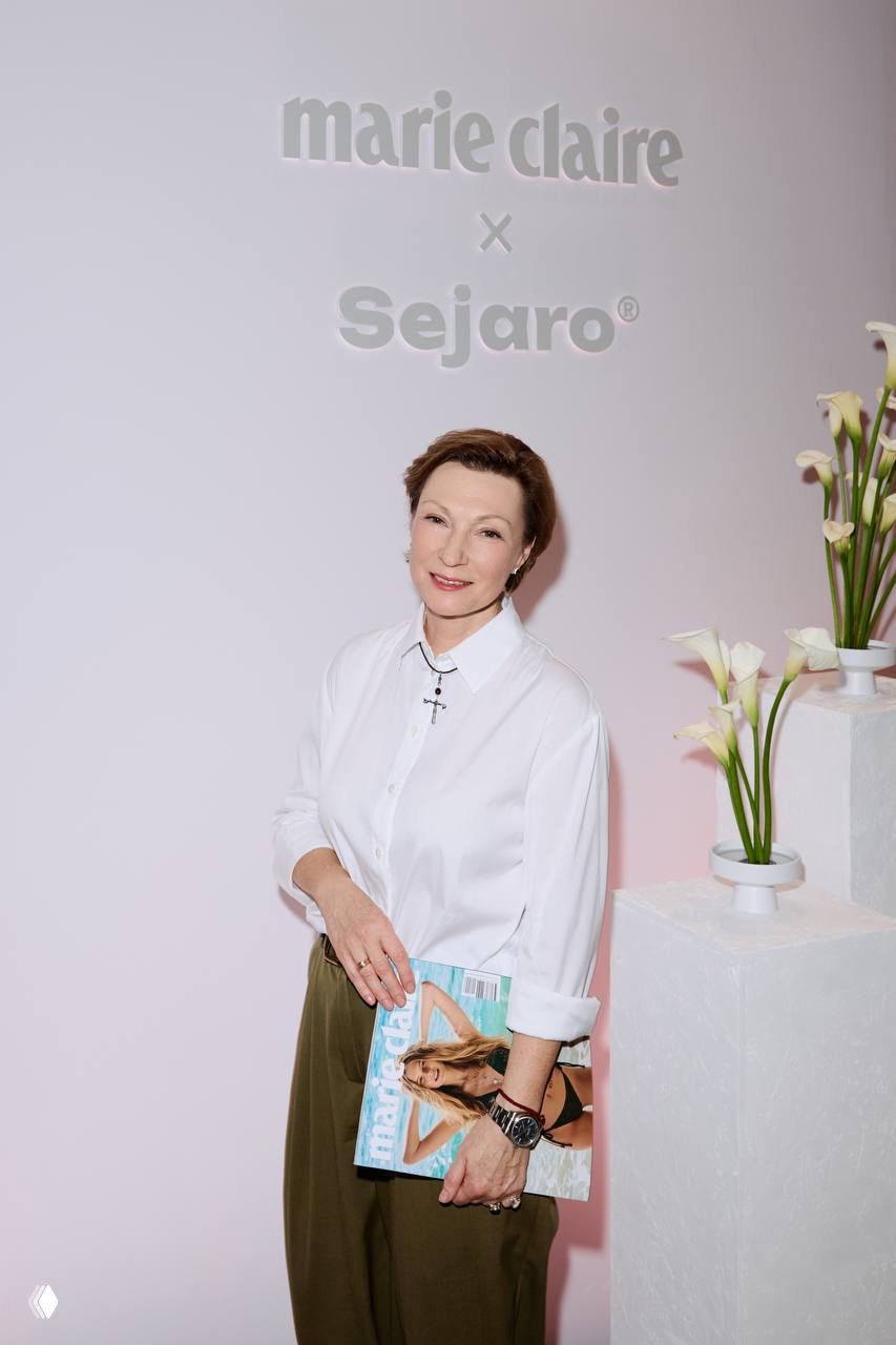 Портретная фотография гостя мероприятия на фоне светлой стены с логотипом Marie Claire x Sejaro, спокойный корпоративный тон.