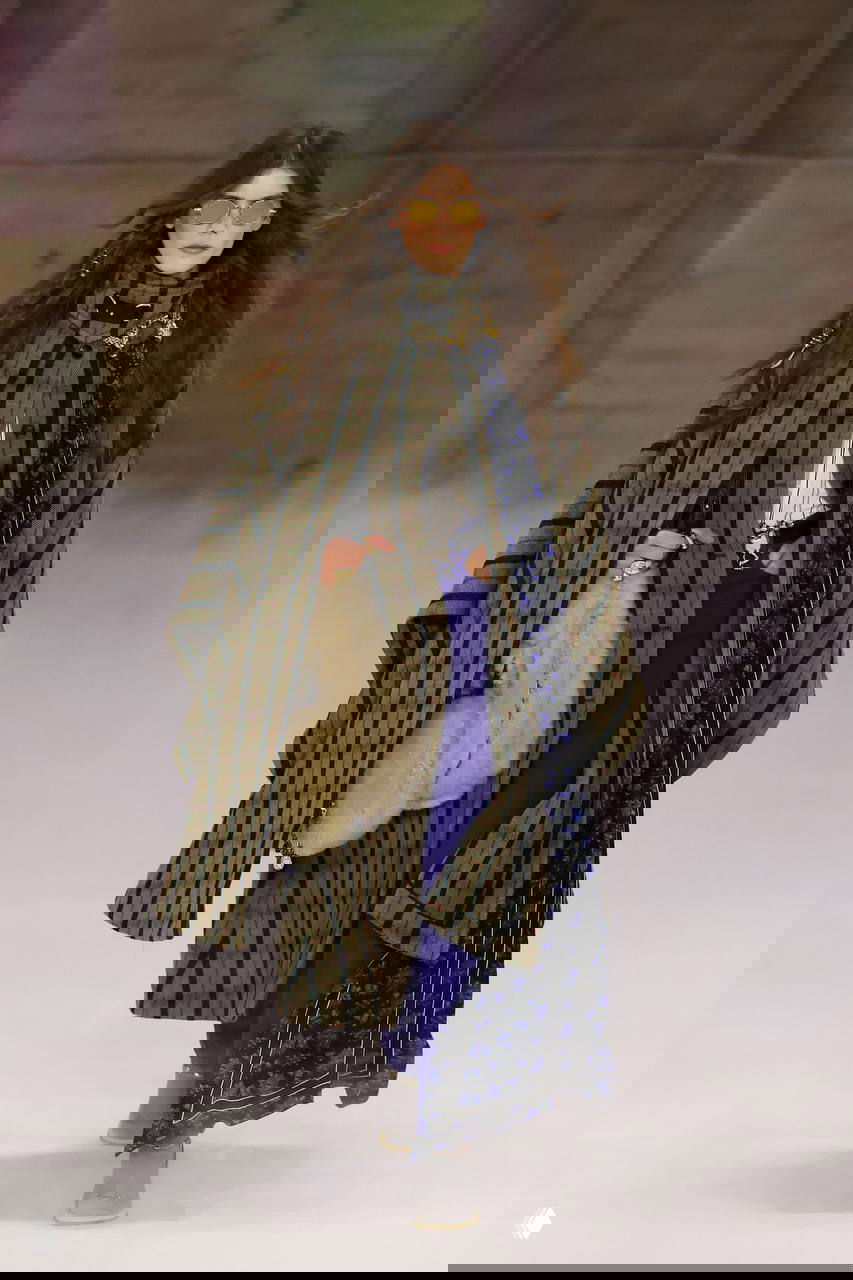 Показывают накидку в широкую полоску и уютную меховую сумку, плащ‑накидка в сочетании с яркими брюками и акцентной текстурой ткани.