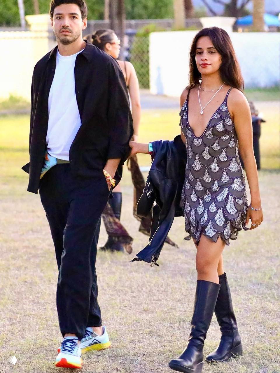 Парень и девушка на фестивале: она в блестящем платье с пайетками и высоких ботинках, они идут по открытой площадке.