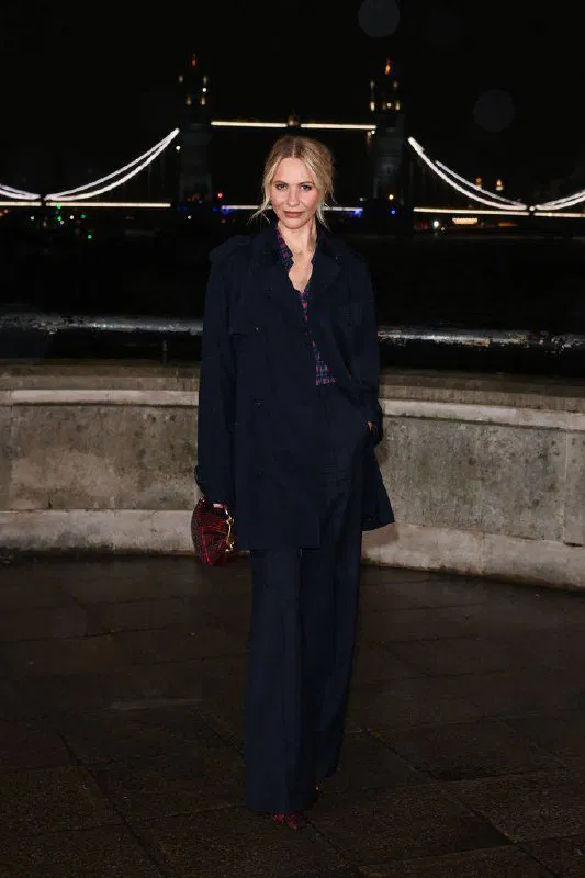 Женщина в тёмном пальто и деловом костюме позирует у набережной ночью, образ в спокойной классике на фоне подсвеченного моста.