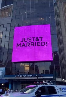 Экран над зданием с яркой надписью «JUST MARRIED» и полицейский автомобиль у входа — городской момент празднования свадьбы в Нью-Йорке.