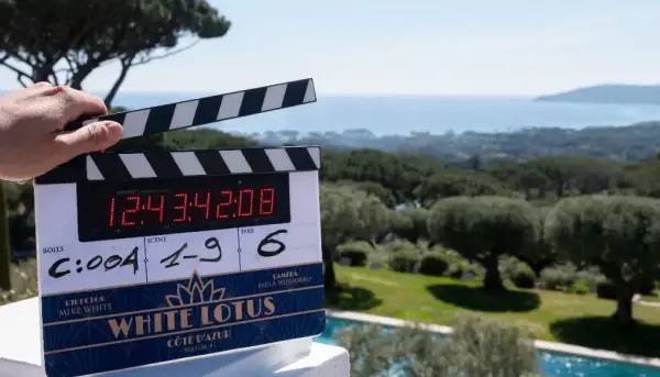 Клэпборд на фоне моря, пальм и побережья — кадр со съёмочной площадки White Lotus на Лазурном Берегу, отмечающий рабочий процесс.