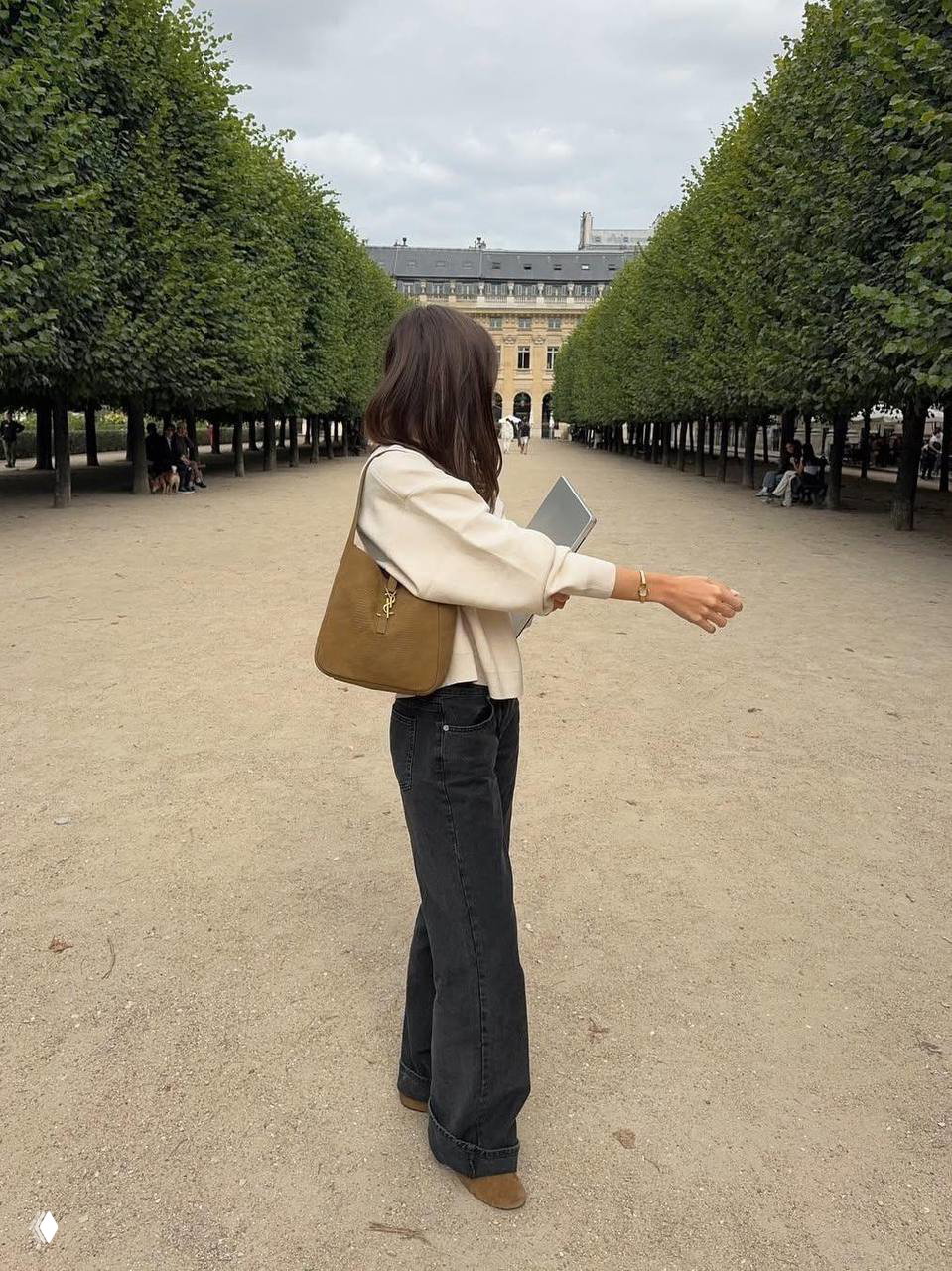 Женщина с сумкой и ноутбуком идёт по аллее парка в светлой одежде — образ мобильной работы и прогулки в городской среде.