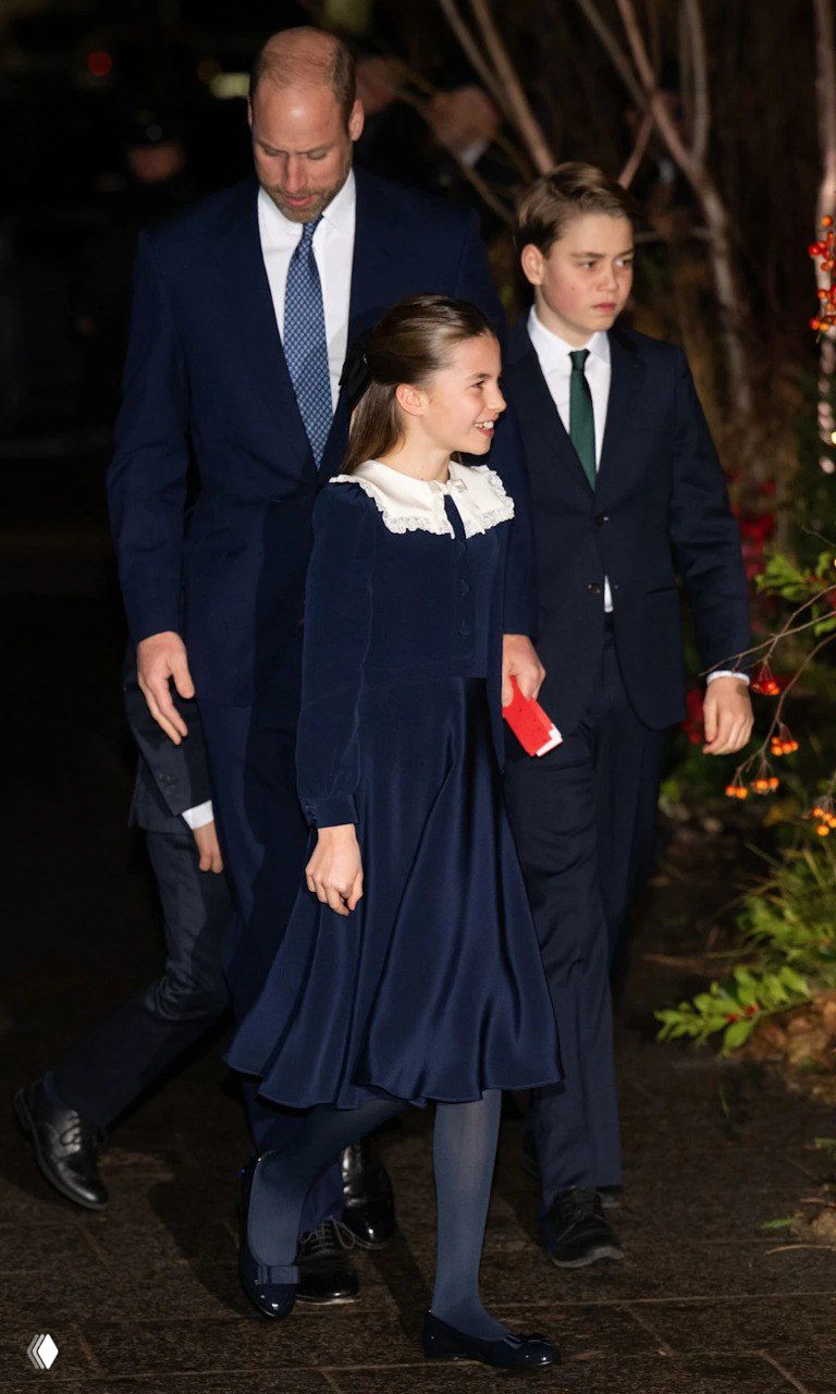 Девочка в тёмно-синем платье и двое юношей в строгих костюмах идут рядом со взрослыми по праздничной аллее