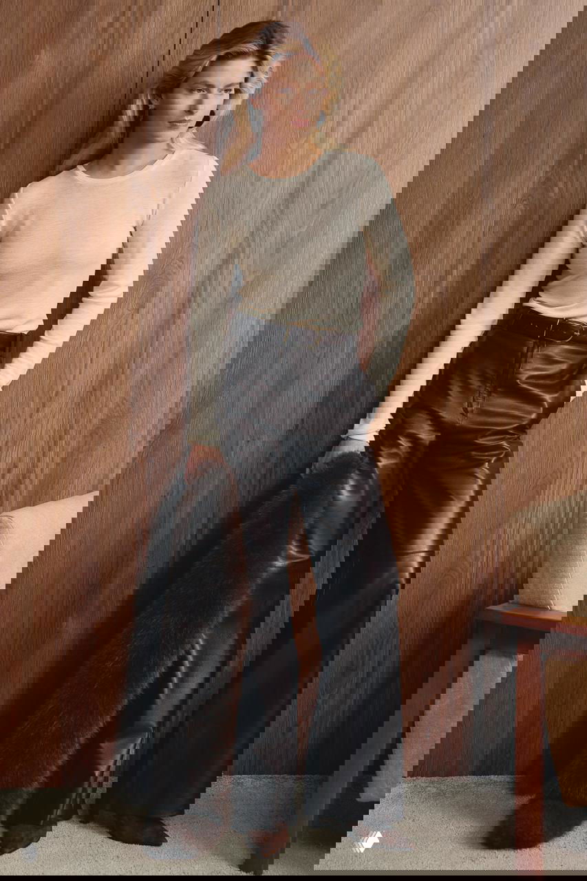 Модель в чёрных кожаных брюках и светлом джемпере, в руках длинный меховой шарф — стилизованный зимний образ на деревянном фоне, фотосессия Marie Claire с акцентом на аксессуары и слоистость.