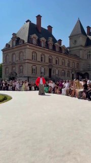 Панорамный кадр показа Balenciaga: дорожка, публика и историческое здание кампуса видны вокруг, модель идёт вдалеке по подиуму.