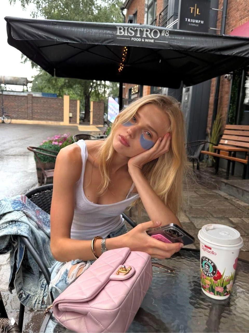 Девушка за столиком кафе на открытом воздухе с розовой сумкой и стаканом кофе, расслабленный летний кадр у бистро.