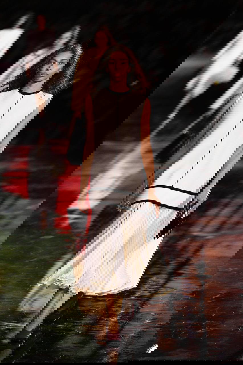 Длинное белое платье с чёрной отделкой на эффектном глянцевом подиуме, сочетание минимализма и воздушности ткани в коллекциях сезона.