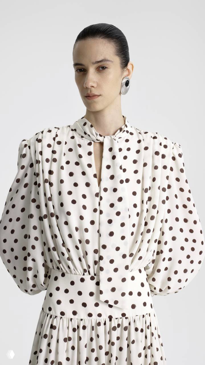 Модель в платье в горох с пышными рукавами и декоративным бантом у горловины — ретро‑эстетика XVIII века переосмыслена в современном крое и фактуре.