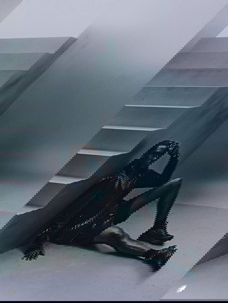 Модель сидит у абстрактной бетонной лестницы в чёрной беговой куртке и шортах; на запястье заметен браслет Whoop, кадр в концептуальном стиле.