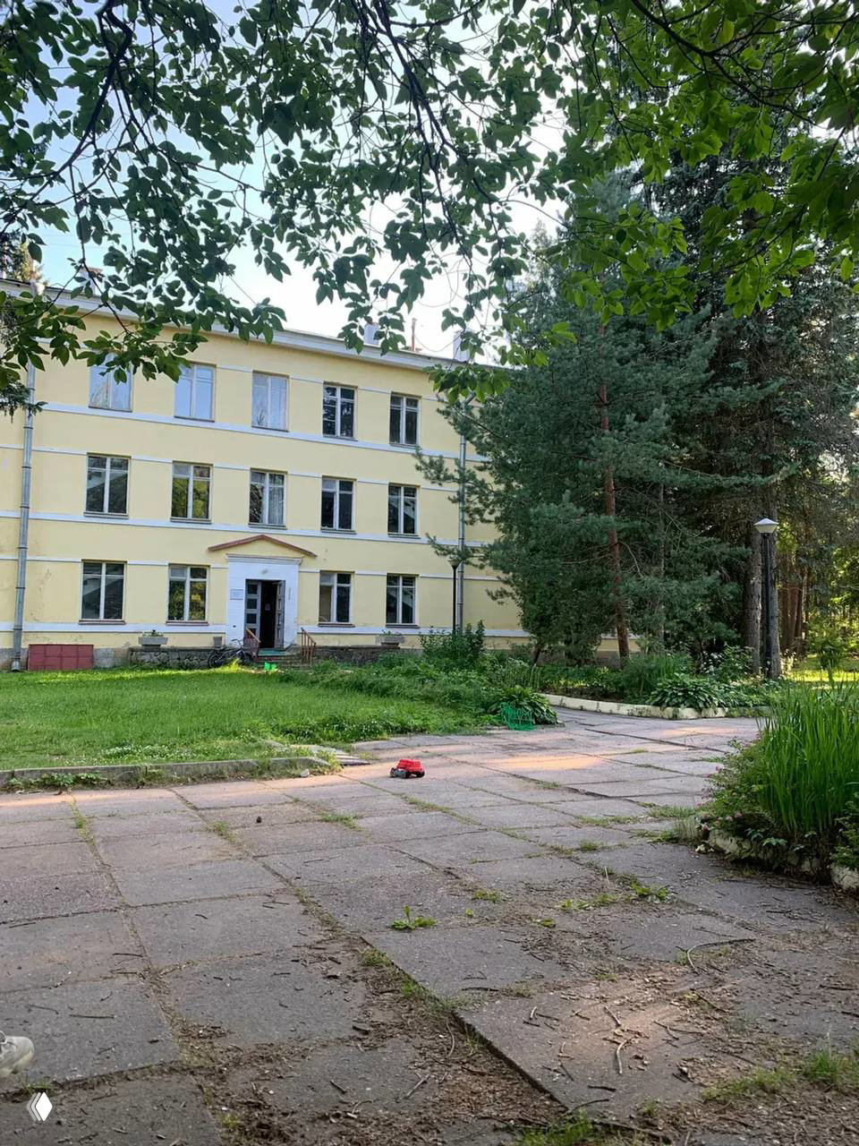 Фасад Дома творчества в Комарове: трёхэтажное жёлтое здание 1950‑х, дорожка и высокие ели на зелёной территории летом