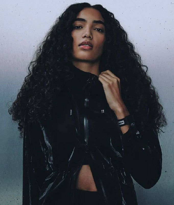 Женская модель в чёрной спортивной куртке и браслетом Whoop на запястье; образ подчёркивает повседневную интеграцию сенсора в спортивную одежду.