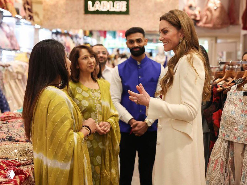 Кейт и гости во время официального мероприятия: видно разноцветные наряды и атмосферу выставочной презентации; изображение содержит визуальные искажения.