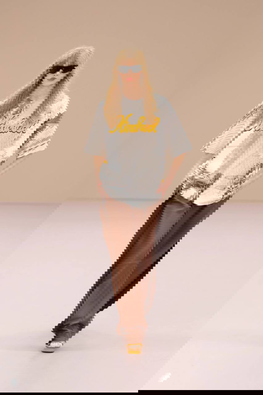 Модель в свободной рубашке и прозрачной юбке на оранжевом подиуме, пример осознанной небрежности и многослойности материалов в коллекциях.