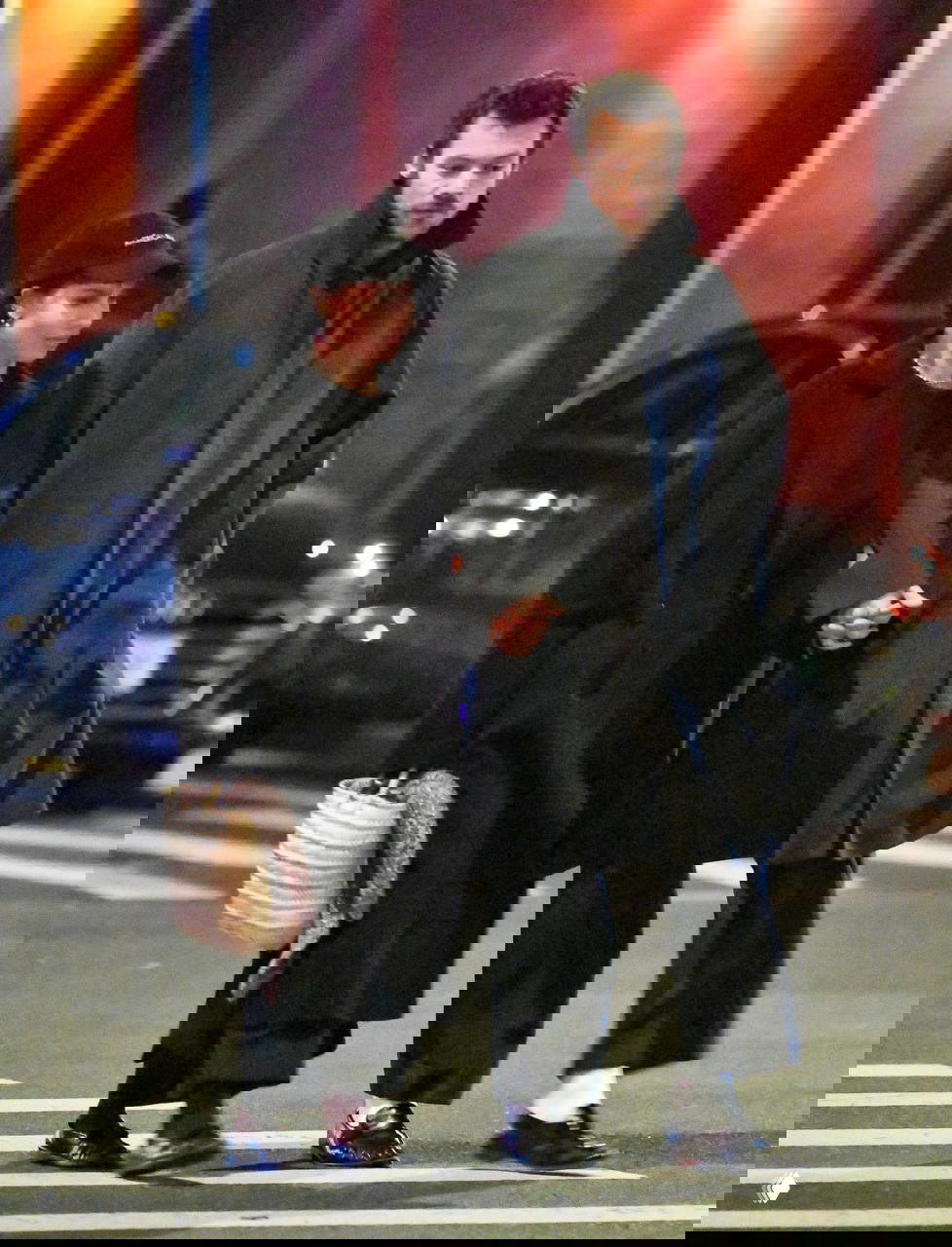 Ночной уличный снимок: пара в чёрных пальто и бейсболке уходит по пешеходному переходу, акцент на их скоординированных образах и объемных пальто.