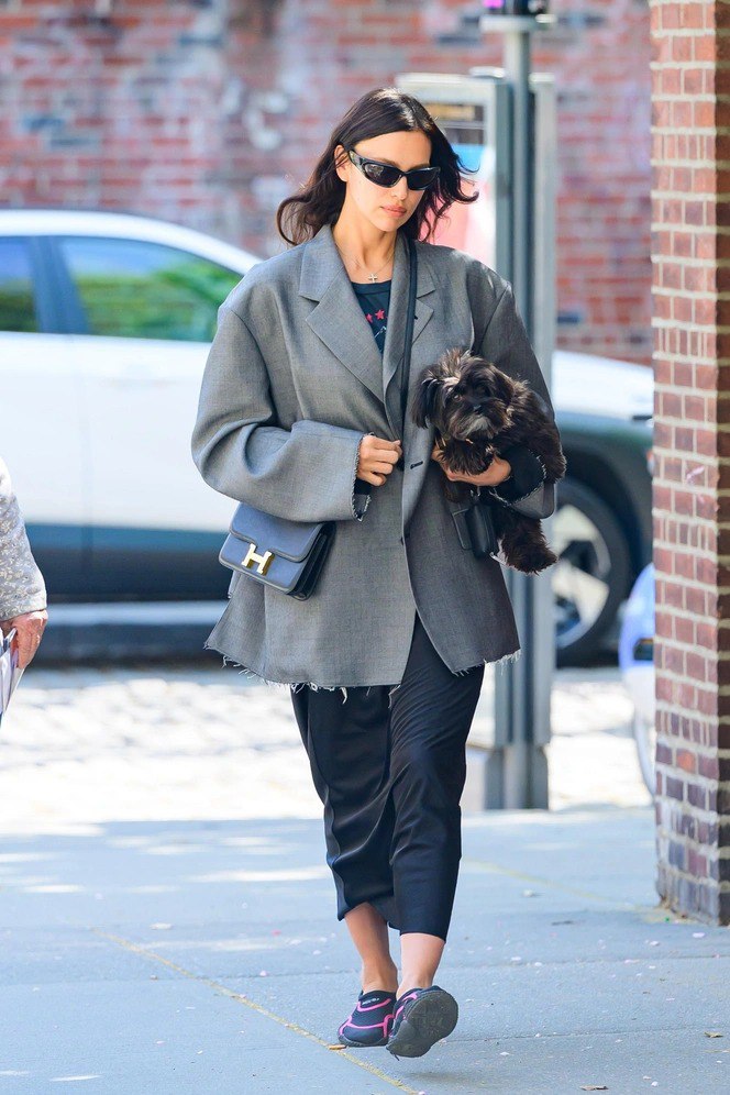 Повседневный образ с оверсайз серым пиджаком, тёмными брюками и маленькой собакой на руках; ретро‑очки в качестве акцента.