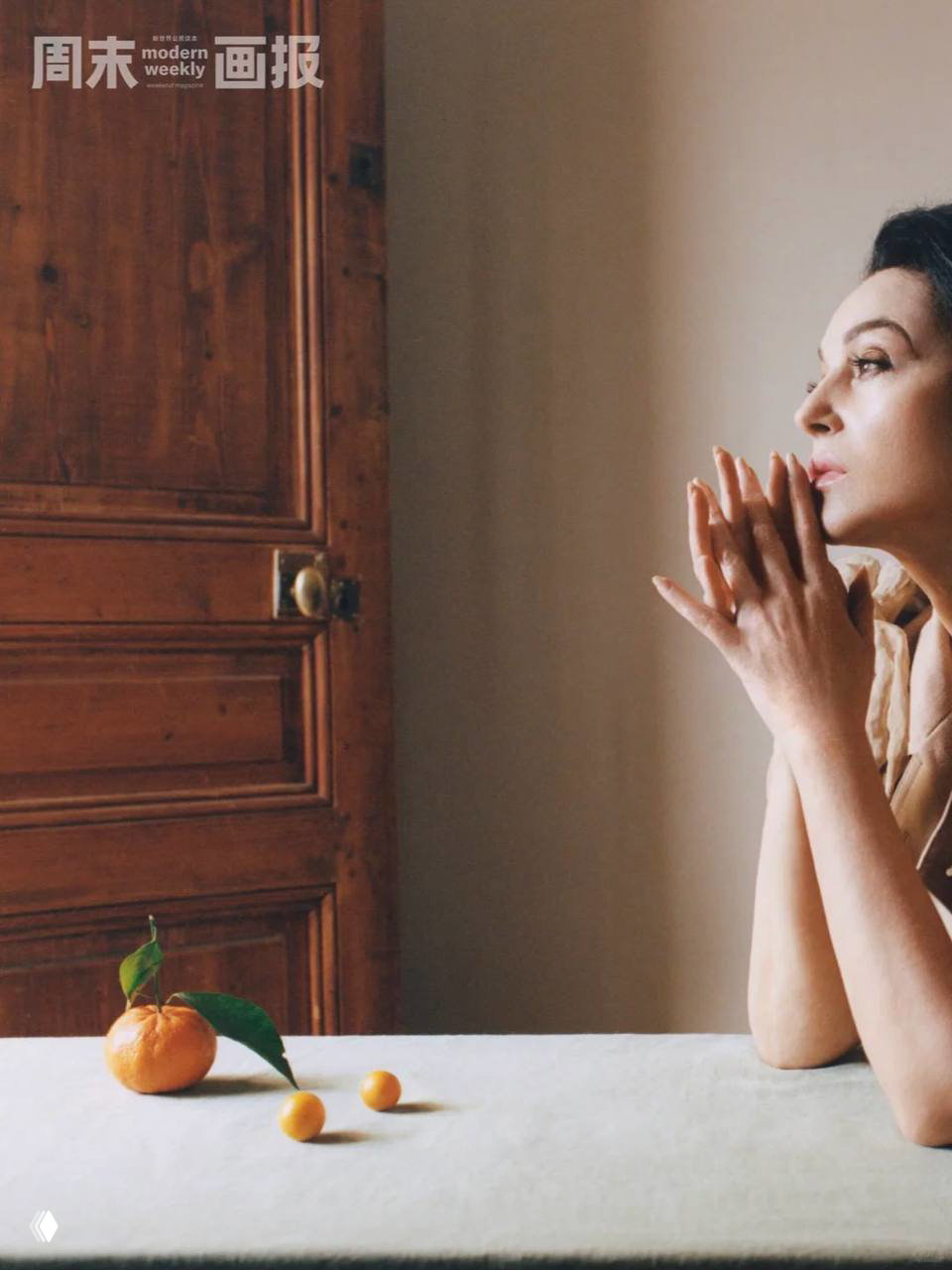 Профильный портрет у деревянной двери: женщина задумчиво смотрит в сторону, на столе рядом — мандарины, интерьер в тёплых природных тонах.