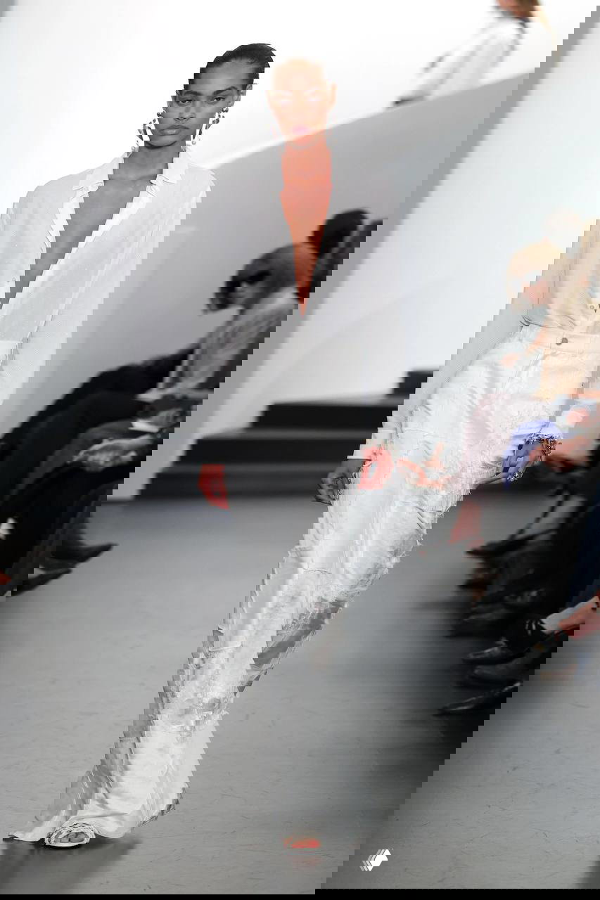 Модель в чёрном укороченном топе и полупрозрачной белой юбке на светлом подиуме — прозрачность и честность материалов как тренд сезона.