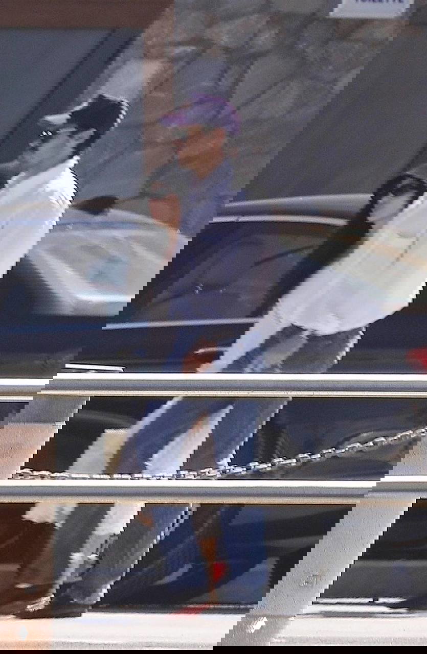 Пляжный или курортный кадр: Гарри в светлой рубашке и джинсах, Зои в лёгком платье и широкополой шляпе — спокойная летняя эстетика пары на прогулке.