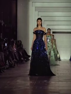 Модель в темно-синем кутюрном платье Tony Ward идет по подиуму в зале с высокими дверными проемами и зрителями по сторонам.