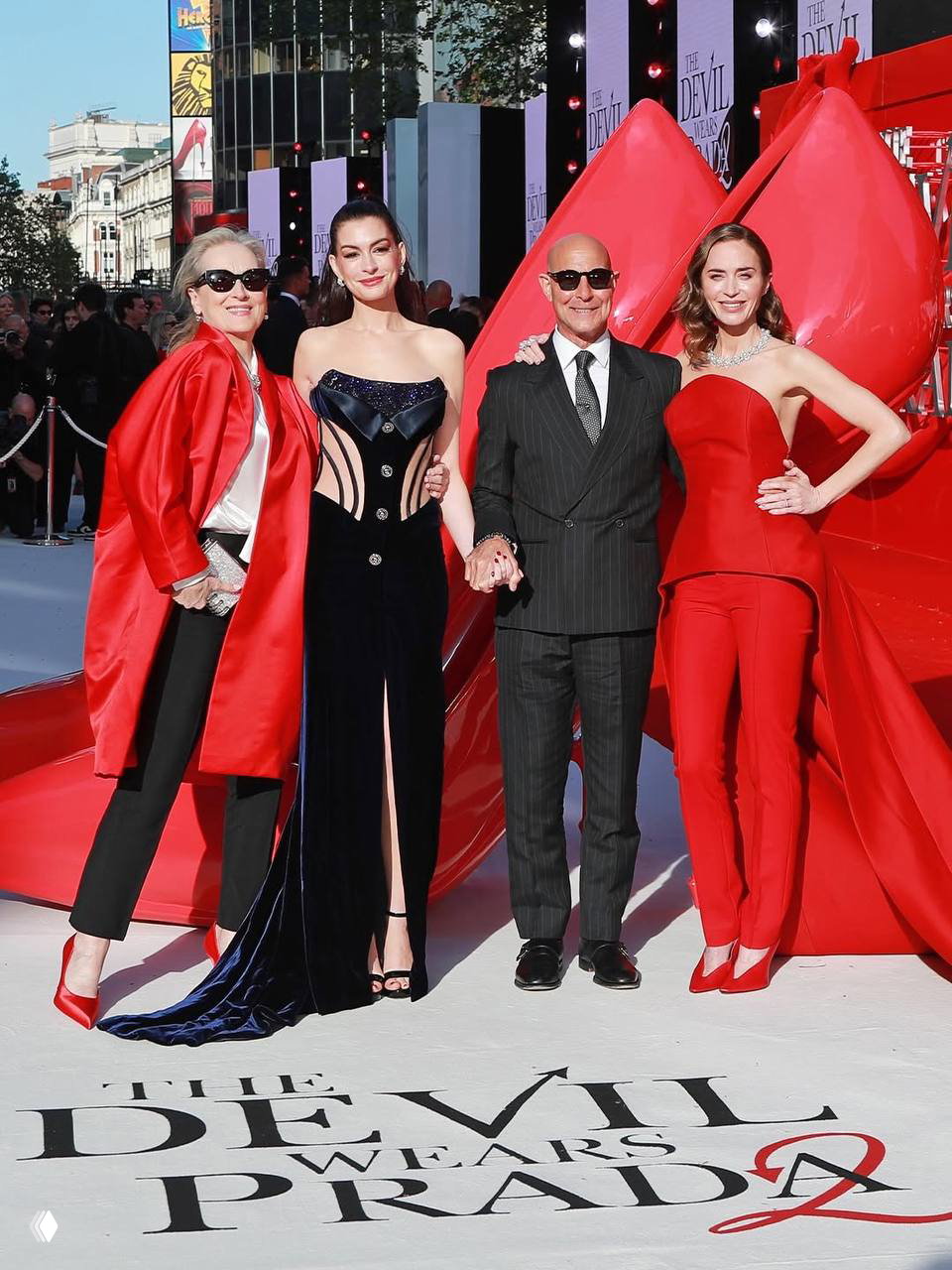 Небольшая группа людей в вечерних образах стоит на белой дорожке с красными арт-декорациями; видна композиция премьеры и гости.