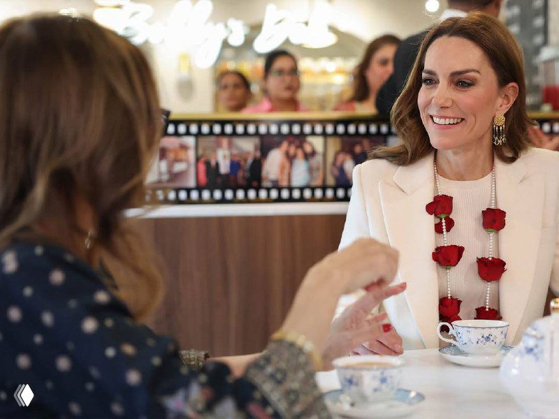 Кейт дарит букет женщине в инвалидной коляске на благотворительном приёме в Южной Азии; платье герцогини светлое, окружающие улыбаются.