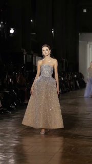 Искрящаяся вечерняя модель в светлом платье из новой коллекции Tony Ward шагает по подиуму под мягким сценическим светом и вниманием зала.