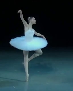 Балерина на пуантах в классической позе на сцене, внимание к линии ноги и положению корпуса, сценический свет уходит в тёмный фон