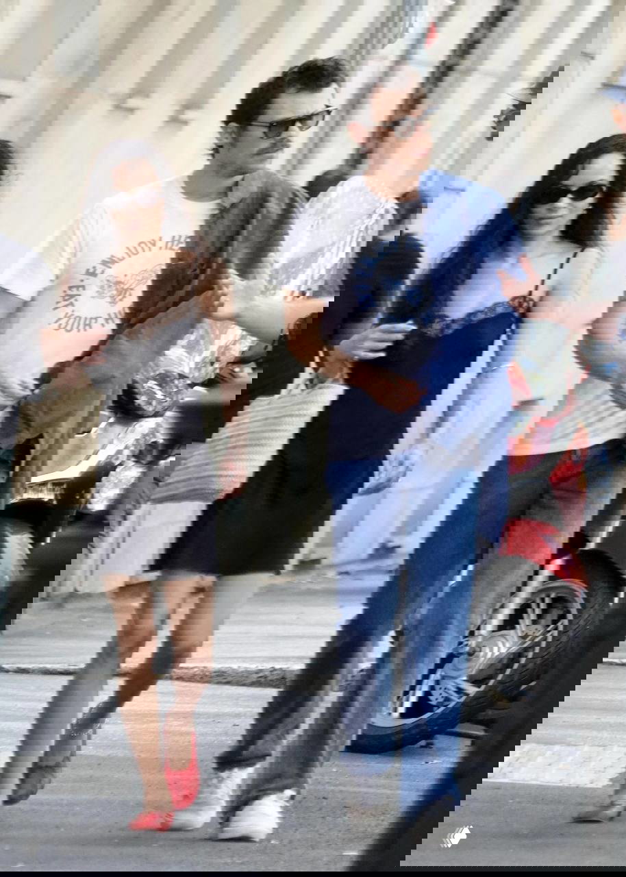 Зои и Гарри идут по улице в простых базовых вещах: Зои в чёрном платье и солнечных очках, Гарри в белой футболке и джинсах — акцент на минимализме.