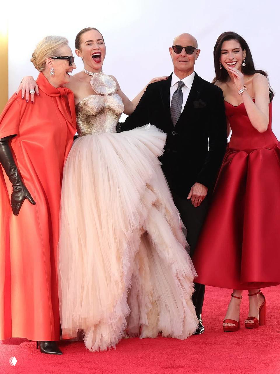 Трое женщин и мужчина на красной дорожке: пышное платье‑тюль, монохромный красный образ и элегантный мужской костюм — кадр со светским мероприятием.