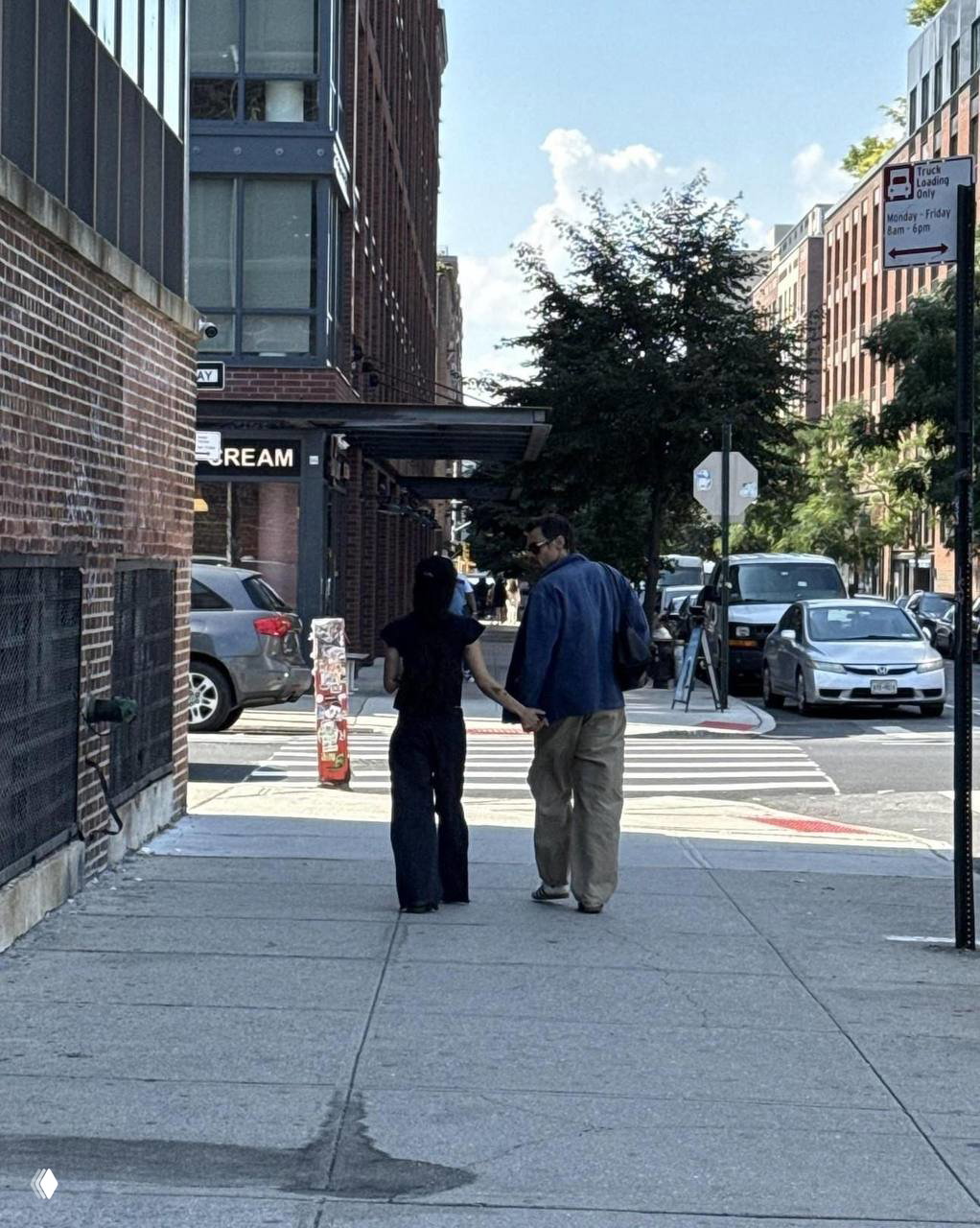 Задний план улицы: пара держится за руку и уходит по тротуару между кирпичных зданий, кадр подчёркивает их неформальную синхронизацию в образах.