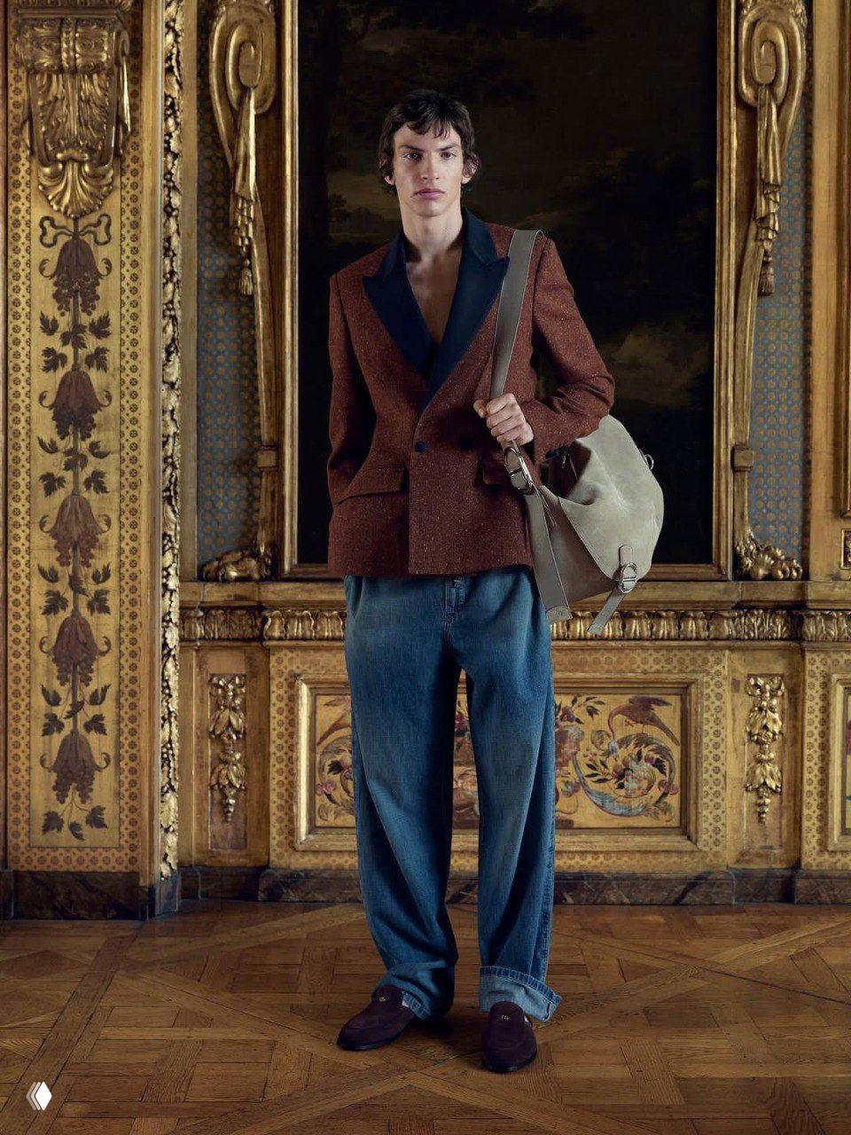 Модель в твидовом пиджаке с чёрными лацканами и мешковатыми джинсами, кадр показывает сочетание классического кроя и расслабленного денима на фоне живописной рамы.