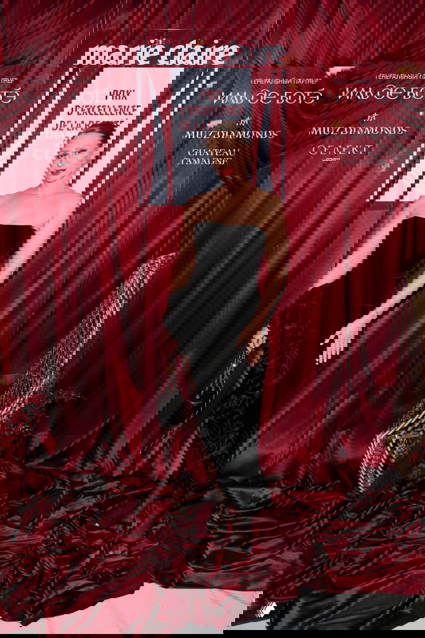 Женщина в чёрном бандажном платье позирует на бордовой красной дорожке у баннера Marie Claire премии 2026.